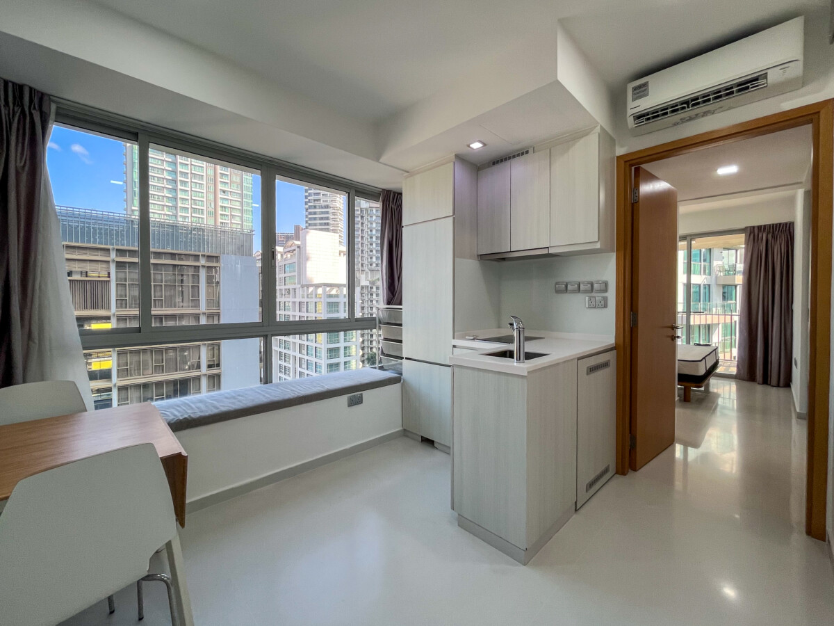 Bright studio kitchen with light wood cabinets, a small island sink, and a window seat overlooking city skyscrapers.