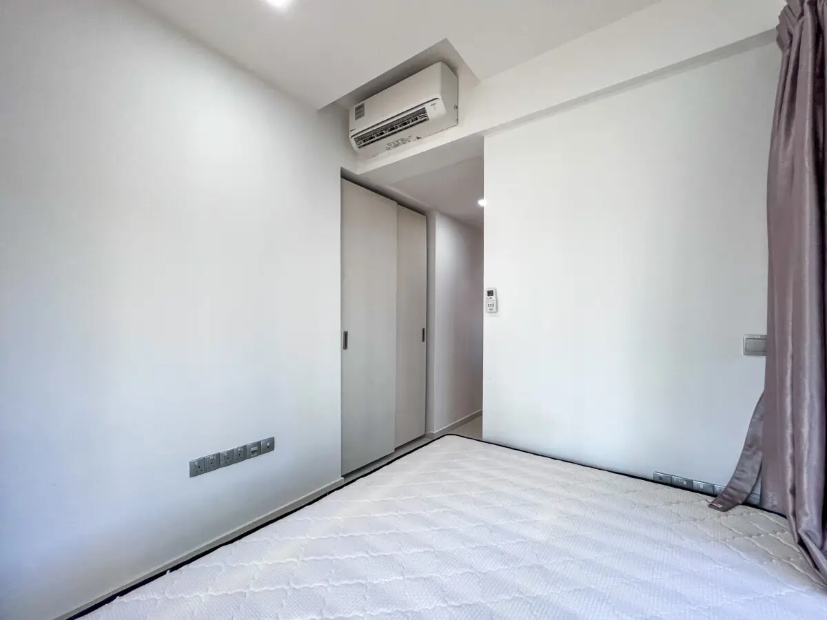 Minimalist bedroom with white walls, wall-mounted air conditioner, sliding closet doors, and a neatly made bed.
