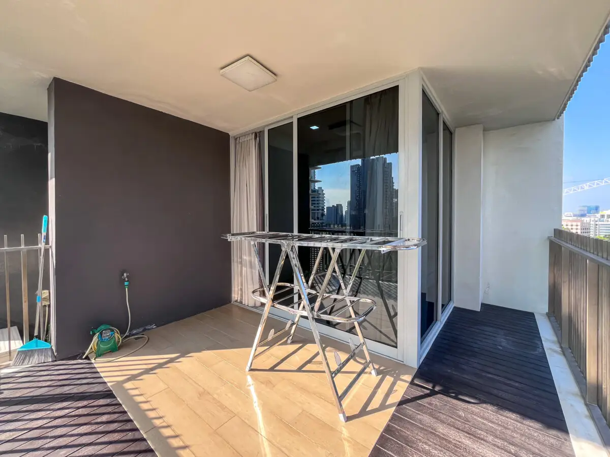 Balcony with a metal folding drying rack near sliding glass doors; city skyline in the background.