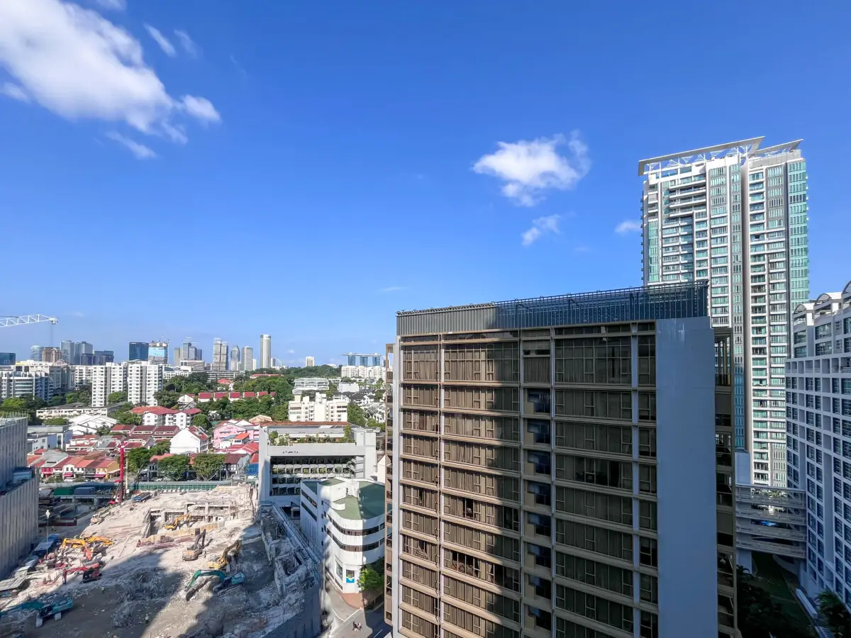 City skyline with tall glass buildings and a construction site in the foreground under a bright blue sky.