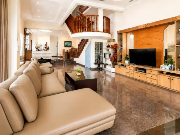 Spacious living room with a beige leather sectional, glass coffee table, and a wooden entertainment unit with a large flat-screen TV.