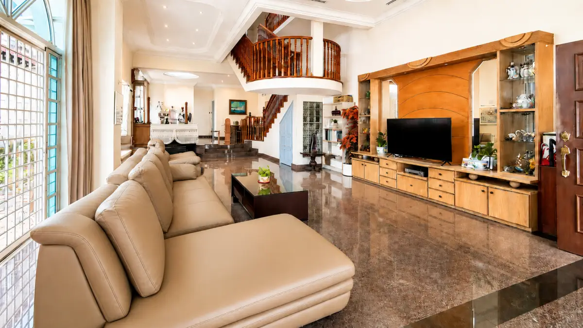 Spacious living room with a beige leather sectional, glass coffee table, and a wooden entertainment unit with a large flat-screen TV.