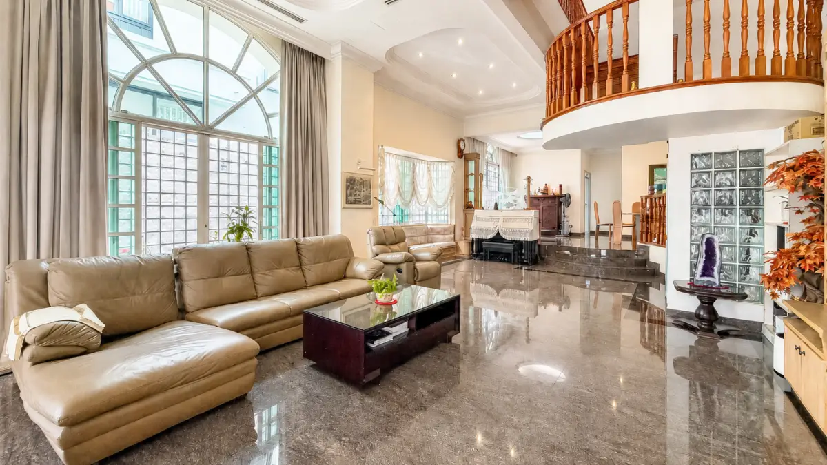 Luxurious living room with a tan leather sectional, glass coffee table, and a large arched window with gray curtains.