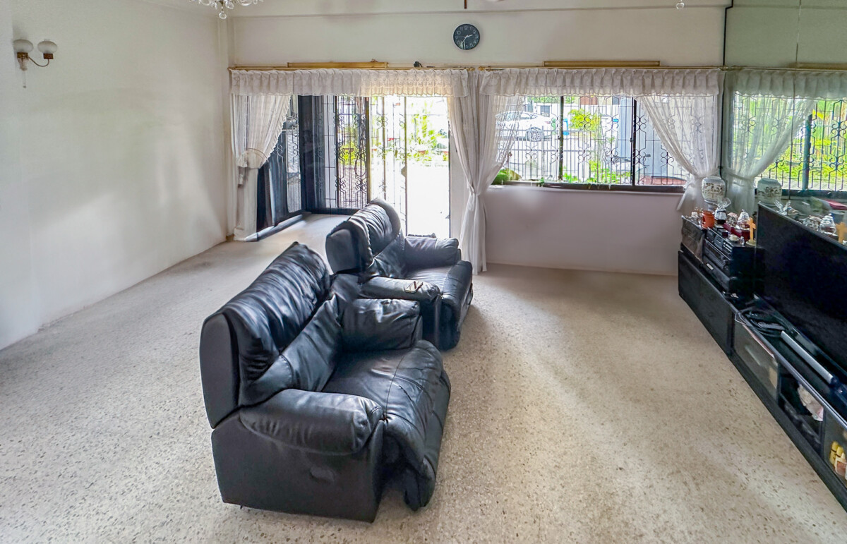 Living room with two black leather sofas facing a TV cabinet, large windows with lace curtains and bright daylight.