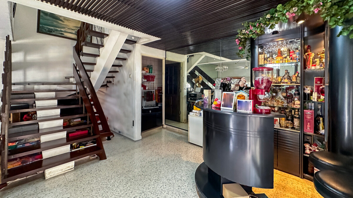 Indoor bar area with a curved black counter, backlit liquor shelves, and a floral garland above the display.