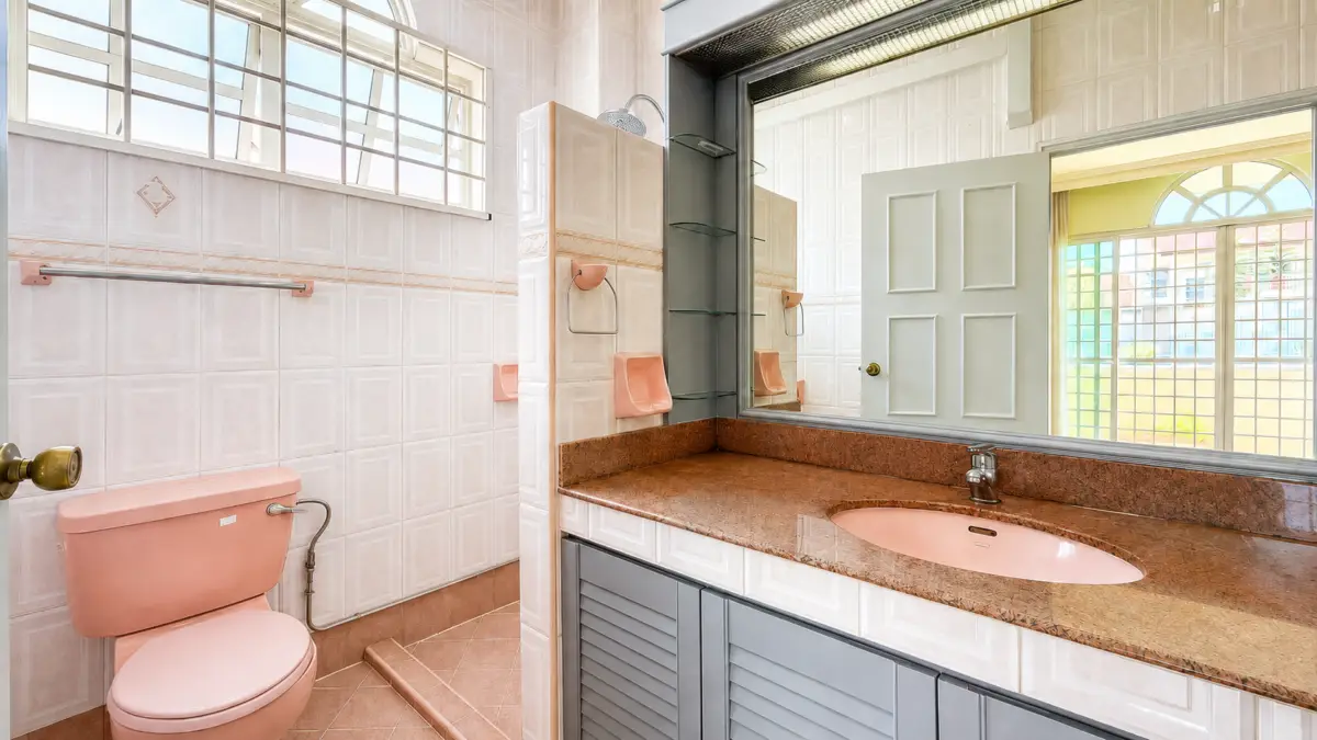 Pink vintage bathroom with matching pink toilet and sink, brown granite countertop, and pale tiled walls with a large mirror above the sink.