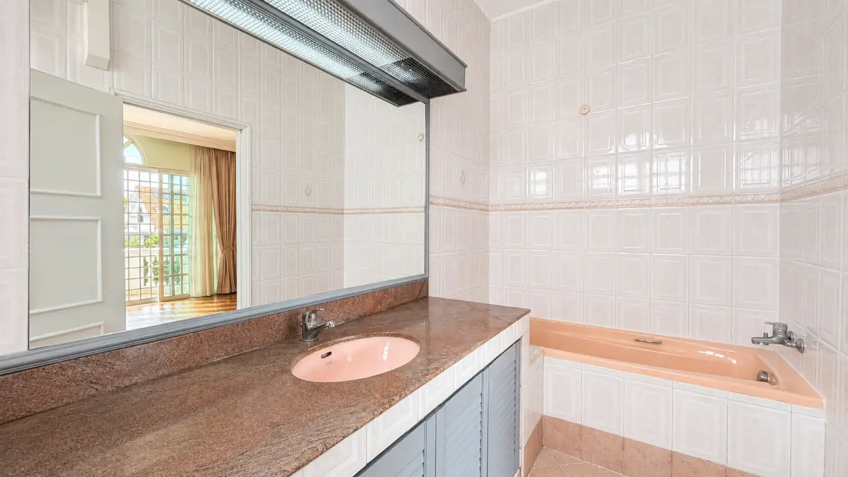 Pink sink and bathtub visible in a tiled bathroom with a brown granite counter and large mirror above the counter.