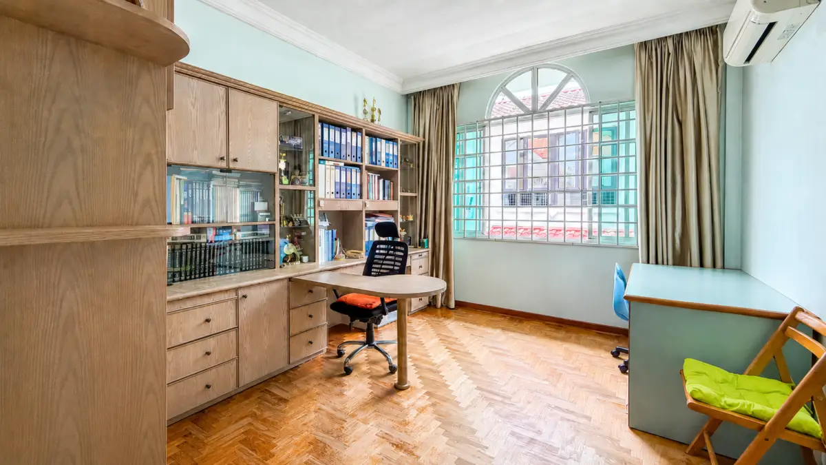 Home office with built-in wooden cabinets, shelves of binders and books, round table, and rolling chair on a parquet floor.