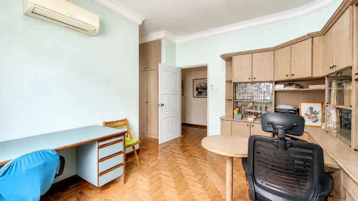 Home office with light blue walls, parquet floor, a long pale desk, and wooden storage cabinets along the wall.