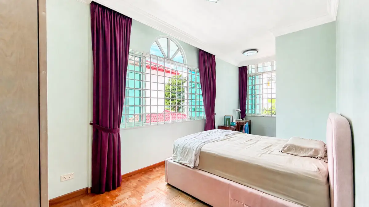 Bedroom interior with a low pink upholstered bed, light bedding, and large windows framed by deep purple curtains in a mint-green room.
