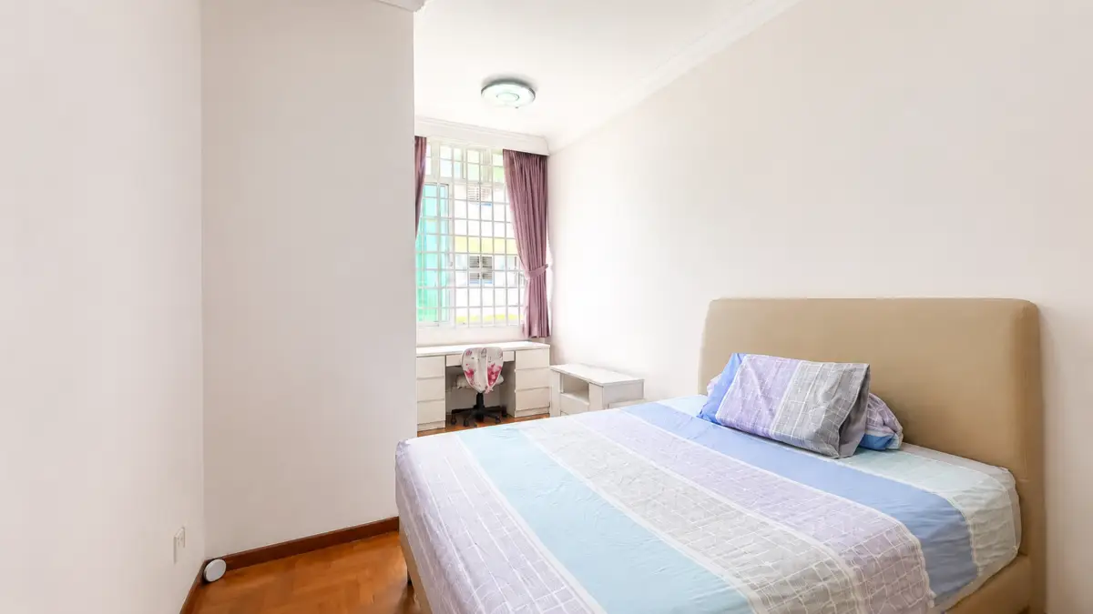 Bed with pastel striped bedding and beige upholstered headboard in a bright, minimalist bedroom by a window with pink curtains and a white desk nearby.