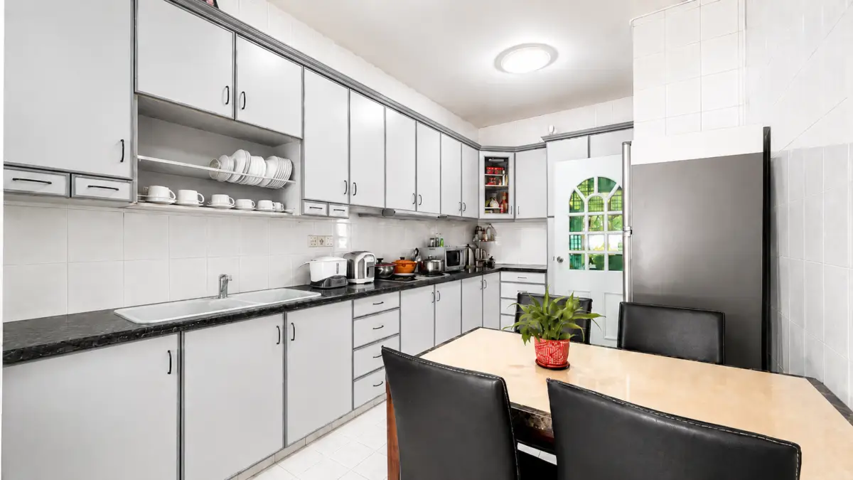 Bright L-shaped kitchen with light gray cabinets, black countertops, and a beige dining table with four black chairs; a potted plant centers the table.