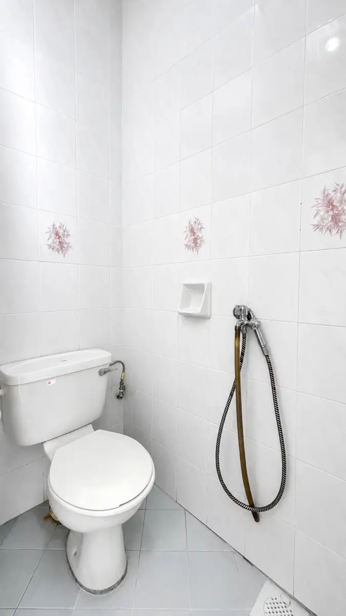 White toilet in a tiled bathroom with a handheld bidet sprayer on the wall and a small wall soap dish nearby.