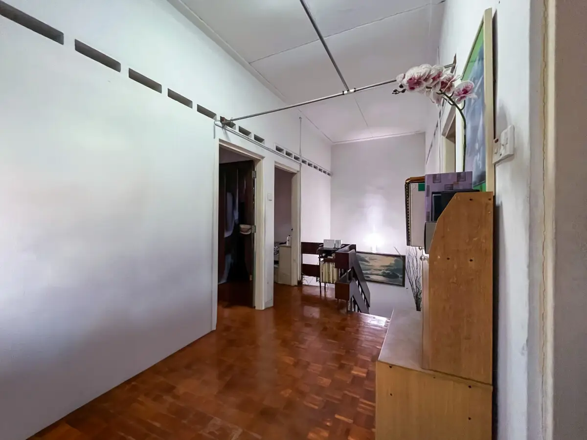 Long hallway in a house with brown parquet flooring, open doorways, and a staircase at the far end; a tall cabinet with a pink orchid on top stands to the right.