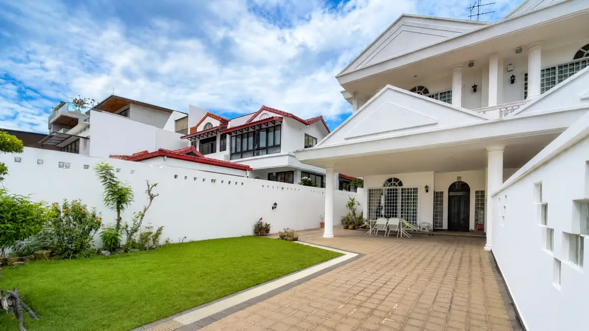 White, two-story villa with a covered patio and outdoor dining area, bordered by a green lawn and potted plants against a blue sky.