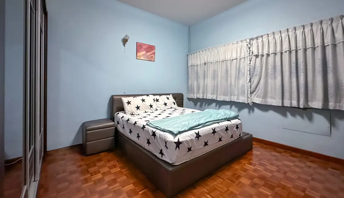 Bedroom with light blue walls, queen bed with star-pattern sheets and turquoise throw on a dark upholstered frame, and a gray nightstand to the left.
