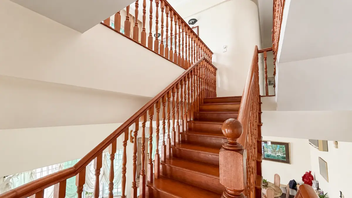 Interior wooden staircase with ornate turned balusters and a large rounded newel post, leading to an upper floor in a bright home interior.