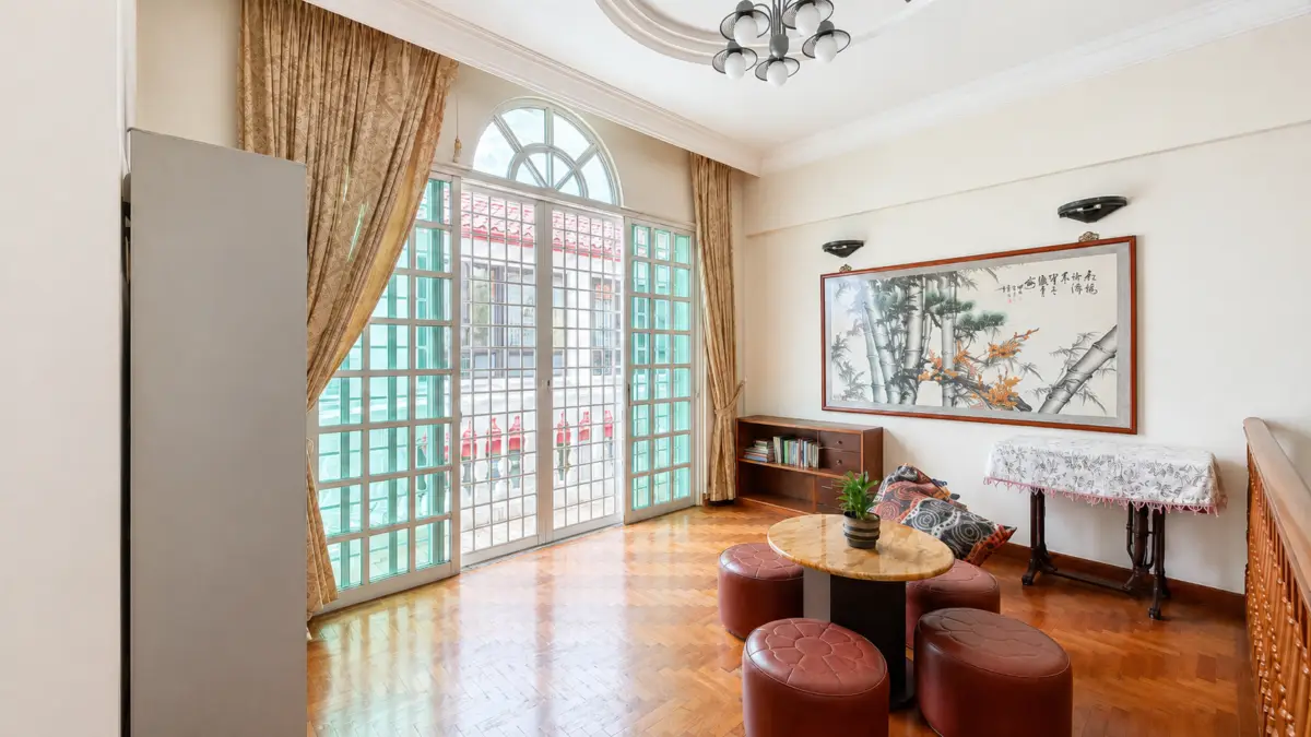 Living room with large glass doors, beige curtains, and a round marble table surrounded by four red cushioned stools.