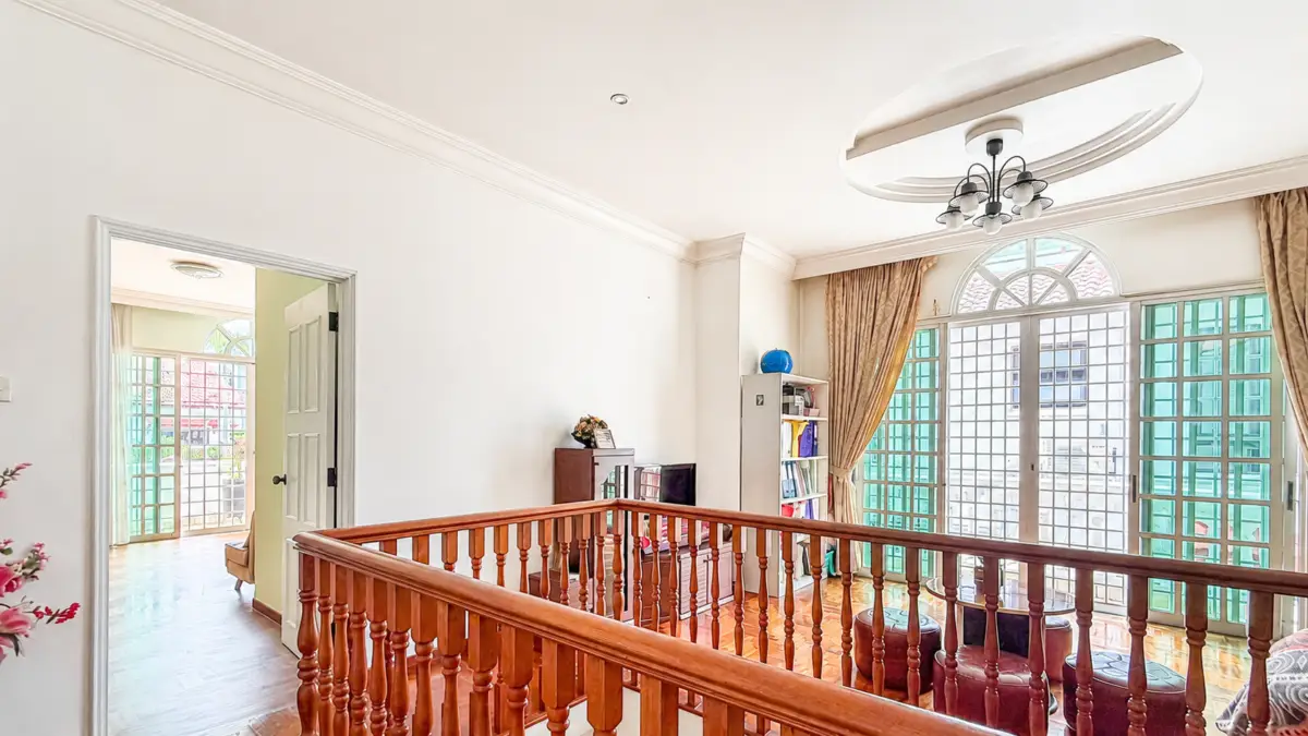 Bright upper landing with a wooden balustrade, large arched windows, and cream curtains beside a living area.