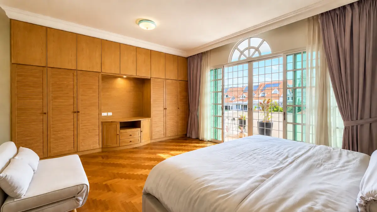 Bright bedroom with a wall of wooden wardrobes, a white bed, and a balcony door with arches.