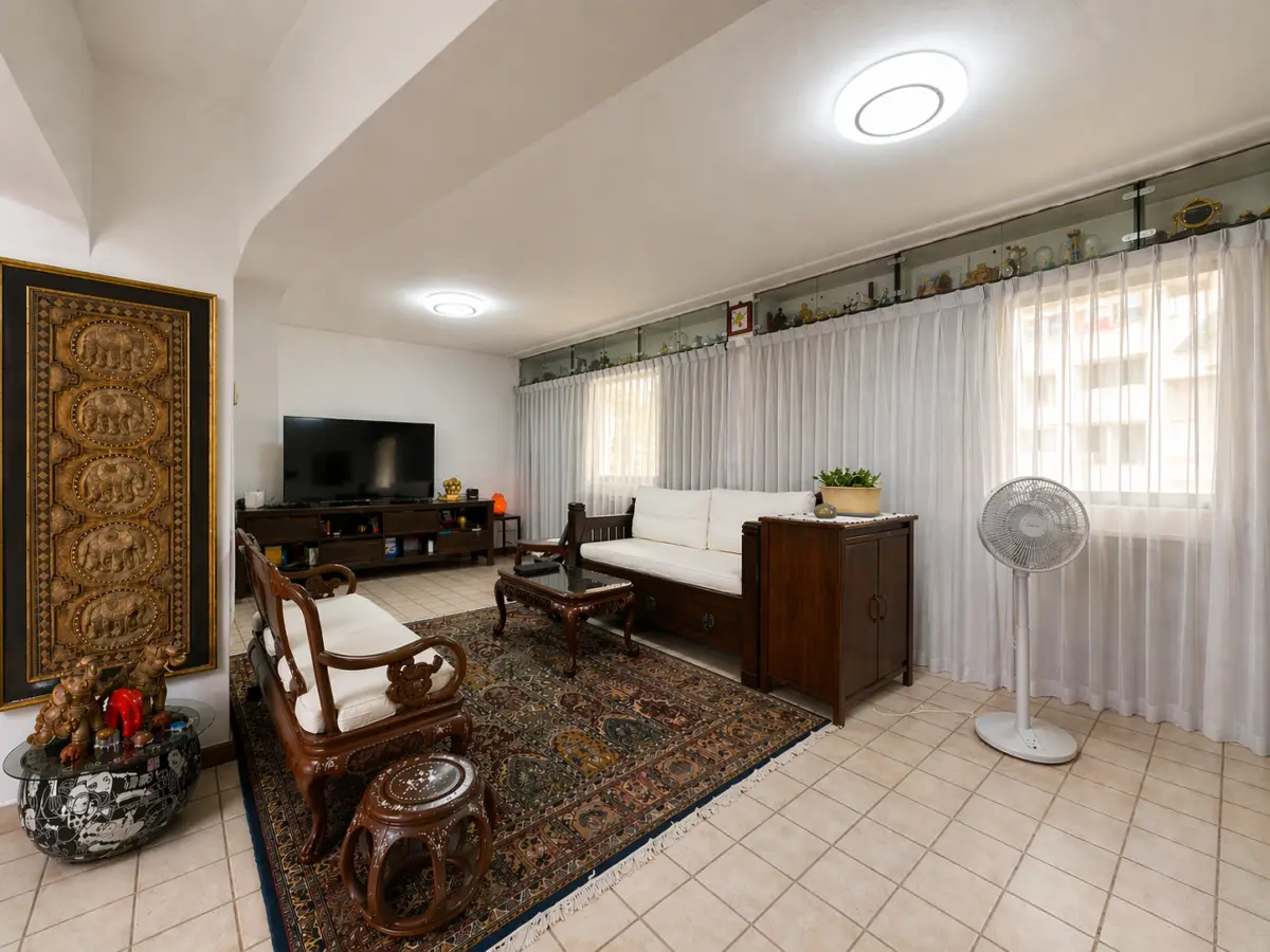 Cozy living room with dark wooden sofa set, white cushions, carved chairs, and a patterned area rug facing a flat-screen TV on a console.