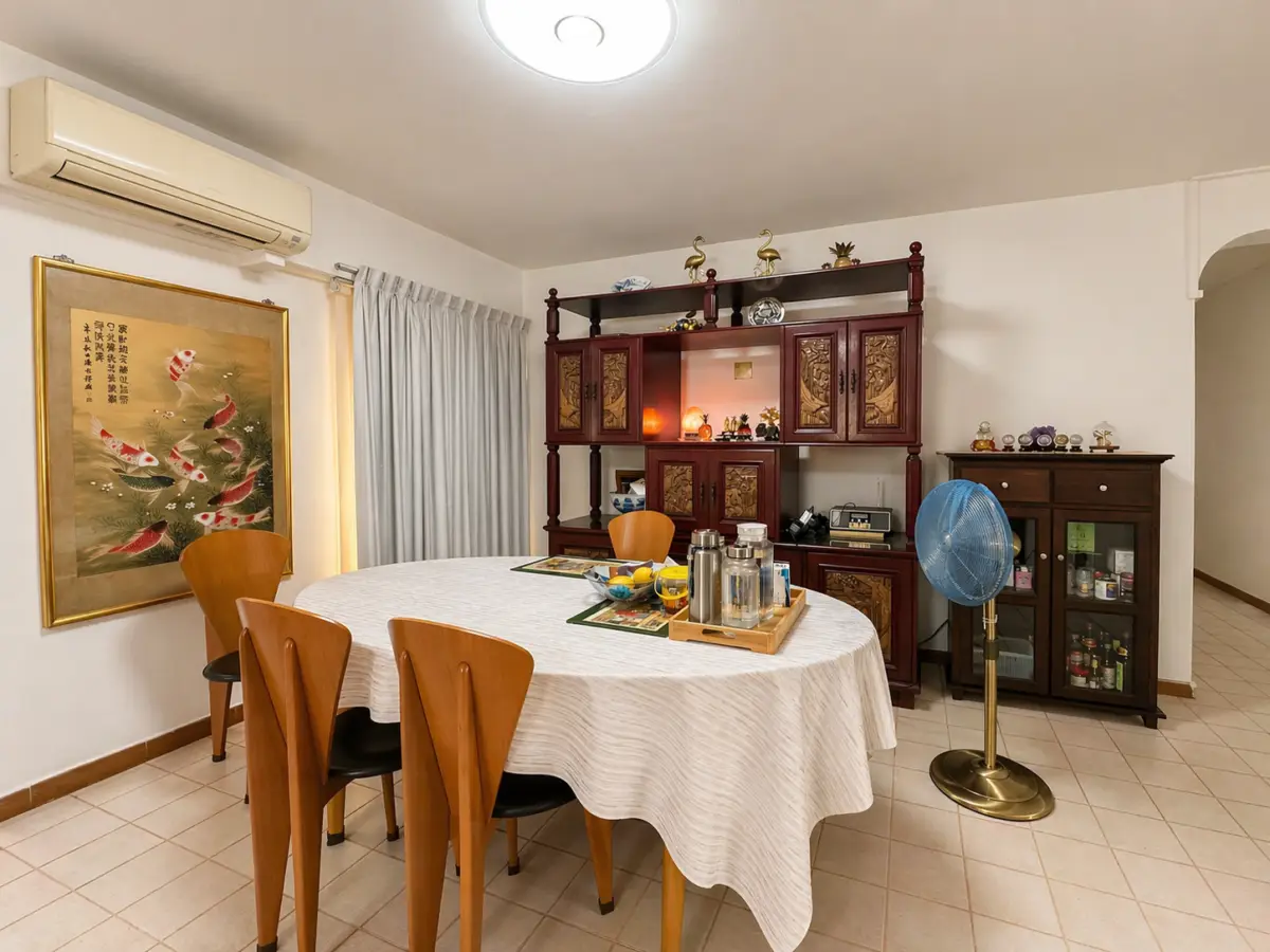 Round dining table with white tablecloth and wooden chairs in a cozy dining room with a large wooden cabinet and a blue floor fan nearby.