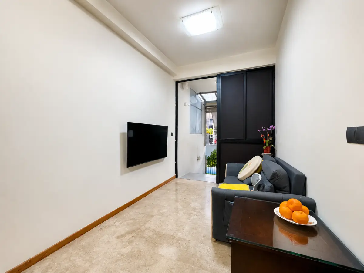 Small living room with a wall-mounted TV, gray sofa, and a glass-top table with a plate of oranges on it.