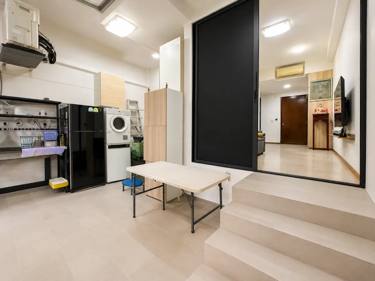 Utility/laundry area with washer and fridge, shelving, and tall cabinets, adjacent to a living area through a large black-framed sliding door.