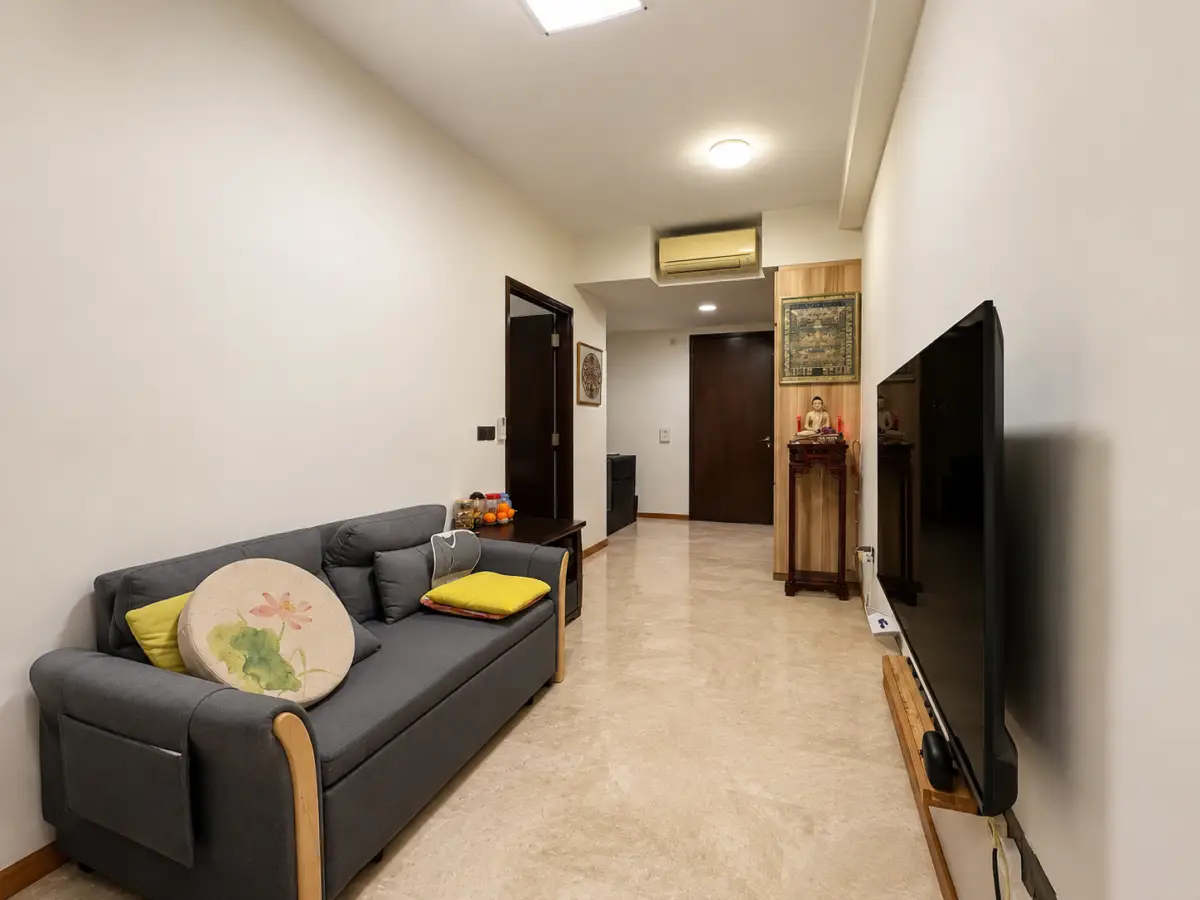 Living room with a gray sofa and colorful cushions facing a large wall-mounted TV on the right; tiled floor and neutral walls.