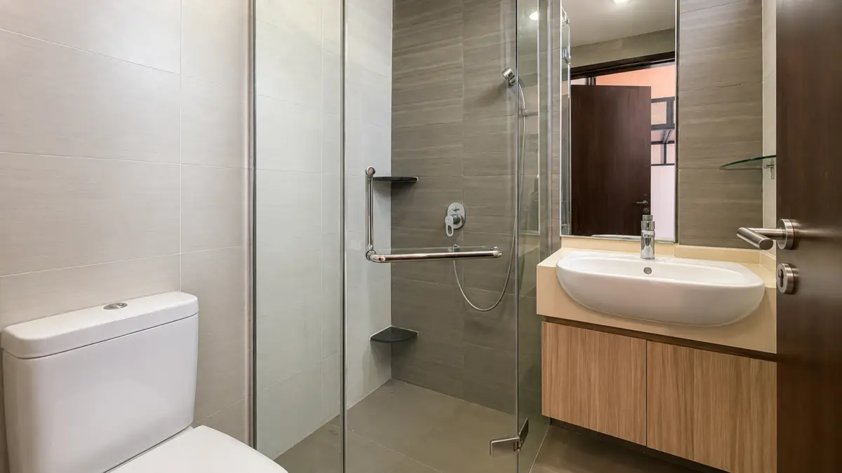 Modern bathroom with glass-enclosed shower, white toilet, and oval sink on a wooden vanity.