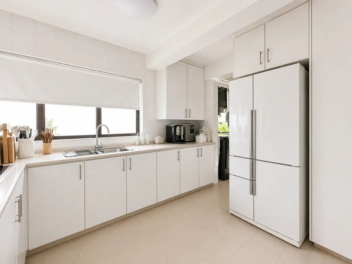 Bright white kitchen with a long counter, double sink under a window, and a large French-door refrigerator.