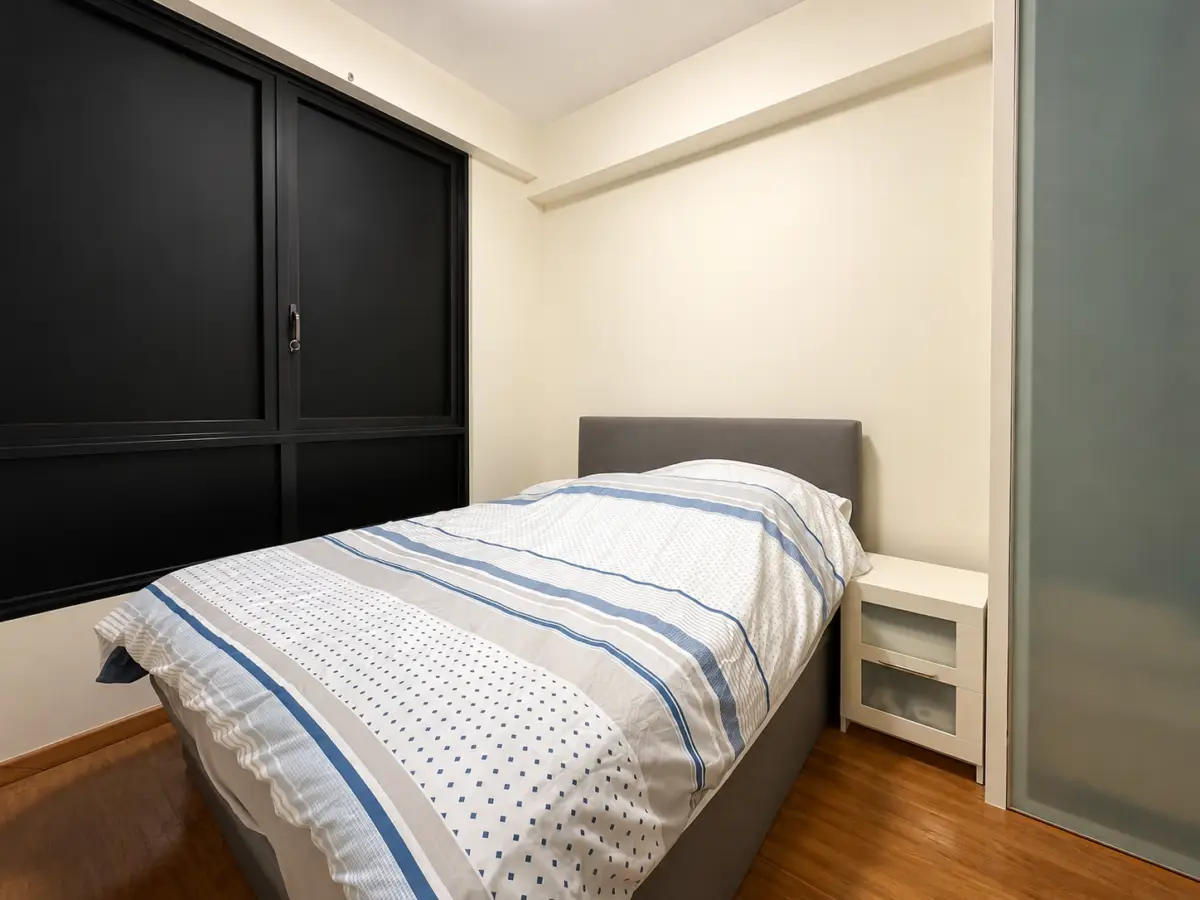 Bedroom with a low, gray upholstered bed and white-nightstand, white bedding with blue stripes, and wooden floor under soft lighting.