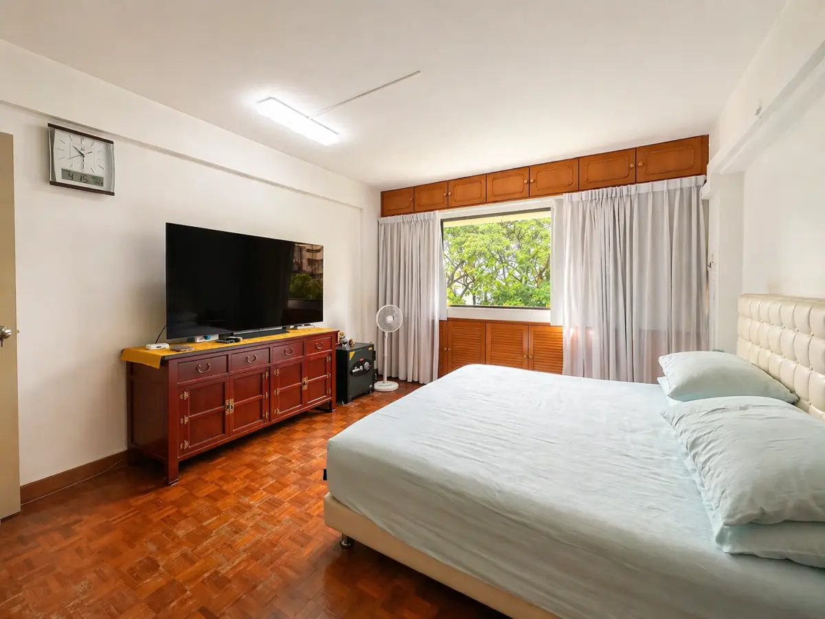 Bedroom with a queen bed on the right, light blue bedding, and a wooden dresser supporting a flat-screen TV.