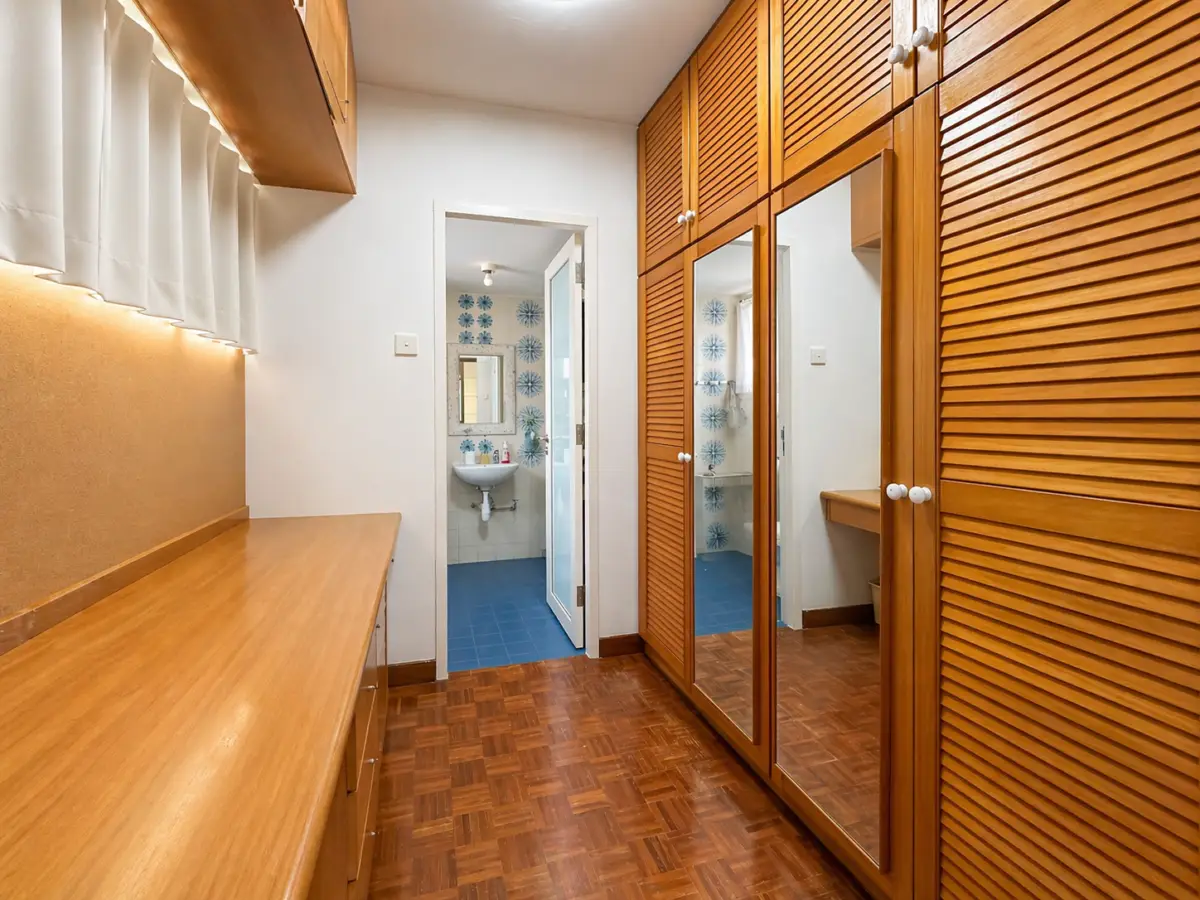 Wood-paneled walk-in closet with a long wooden countertop and mirrored wardrobe doors; doorway opens to a blue-tiled bathroom.