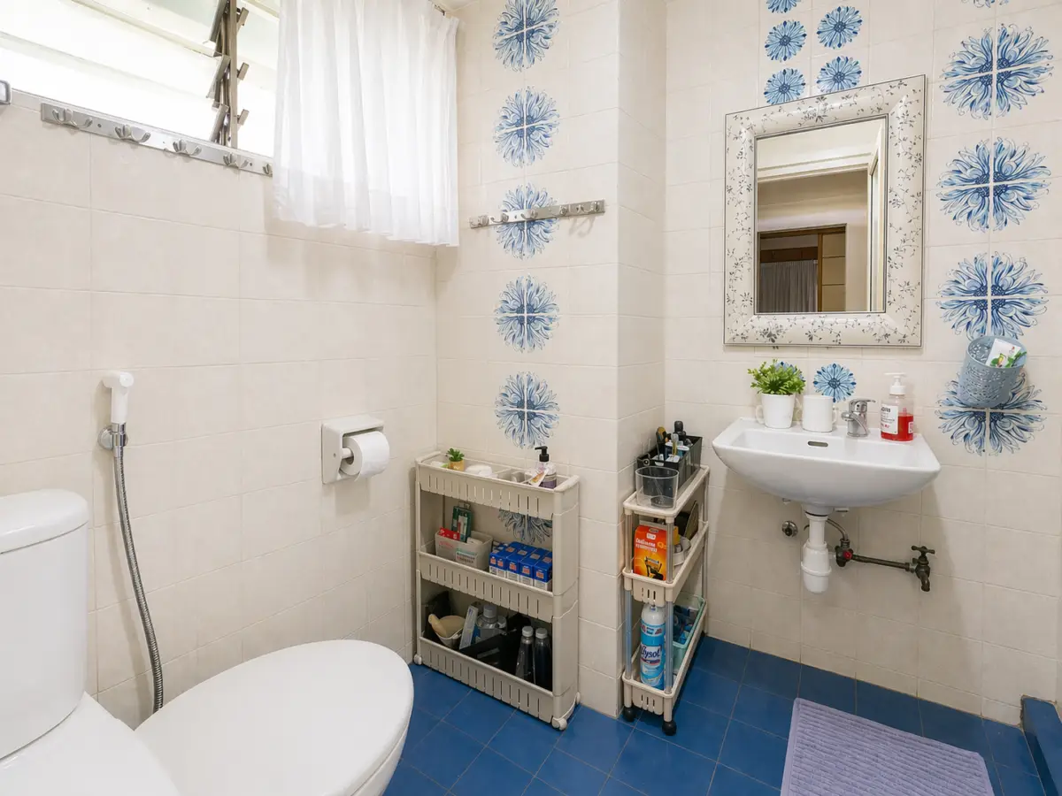 A bright bathroom with white fixtures, blue floral tiles, and a wall mirror above a sink; a toilet and cleaning cart are nearby on a blue-tiled floor.