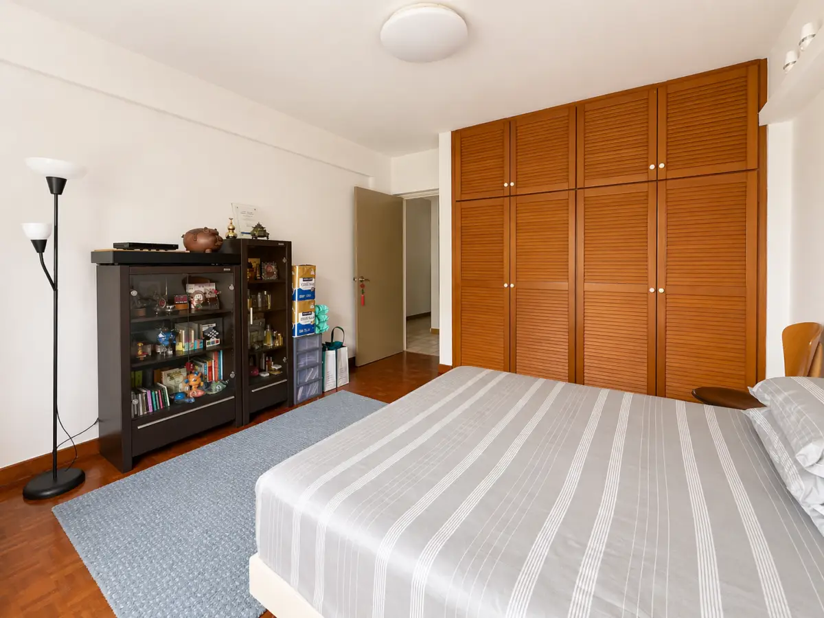 Bedroom with a large wooden sliding-closet wardrobe, a bed with a gray striped cover, and a blue rug on polished wood floors.