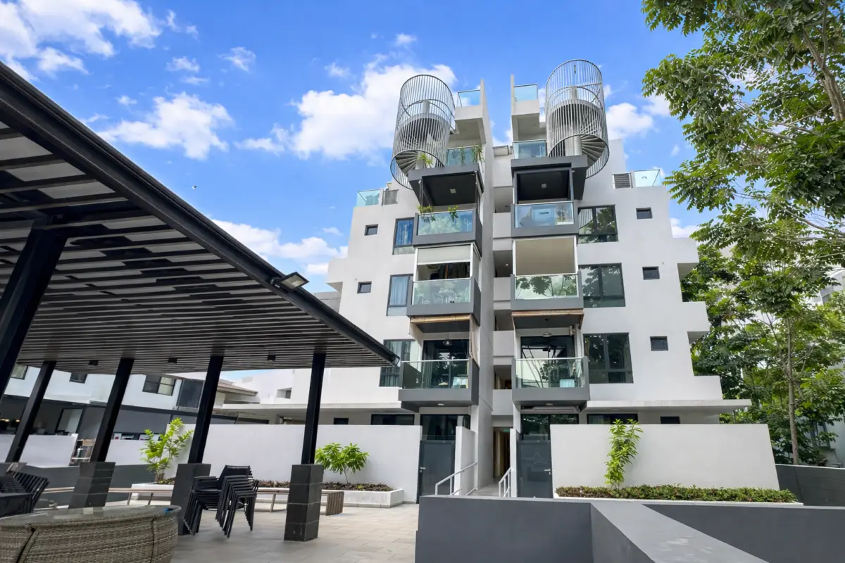 Modern multi-story residential building with glass balconies and spiral rooftop structures under a blue sky.
