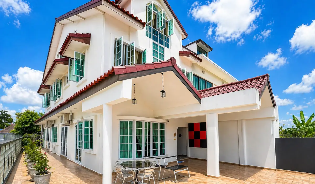 White multi-story house with red-tiled roof and many green-framed windows under a bright blue sky; tiled patio with glass table and chairs divided by a covered entryway.