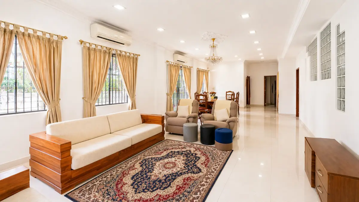 Bright living room with beige sofa, brown wood accents, and a patterned rug near large windows with gold curtains.