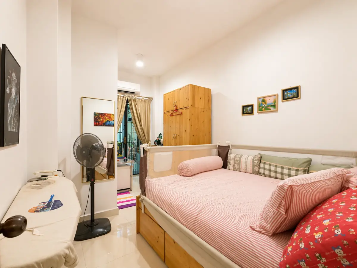 Cozy bedroom with a wooden double bed, pink striped bedding, bolster, and multiple pillows; wardrobe and fan nearby.