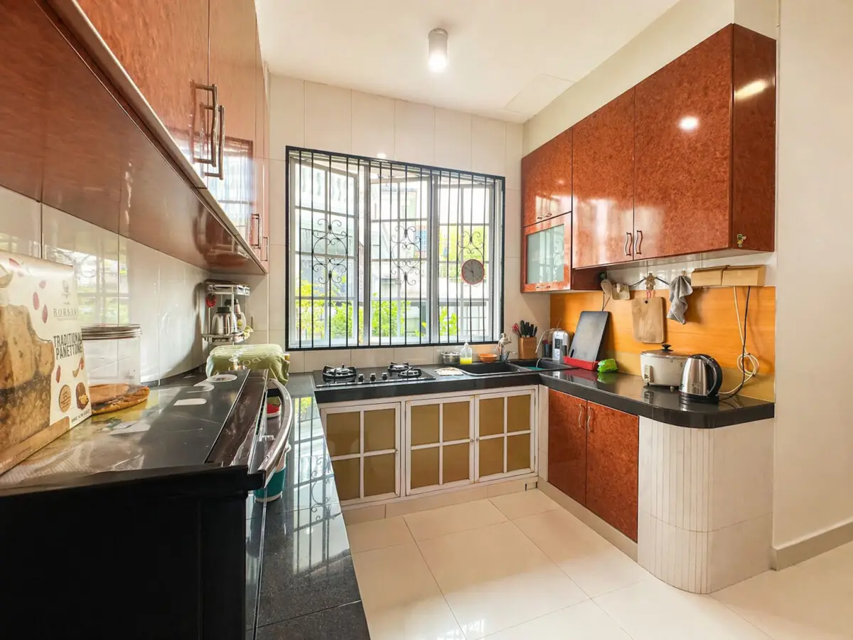 Bright U-shaped kitchen with reddish-brown cabinets, black countertops, and a large window with decorative bars above the sink and stove area.