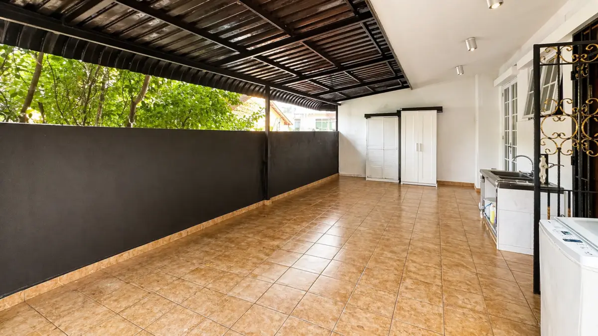 Covered outdoor patio with brown tile floor, black privacy wall, and a laundry area featuring sink, cabinets, and washing machine on the right.