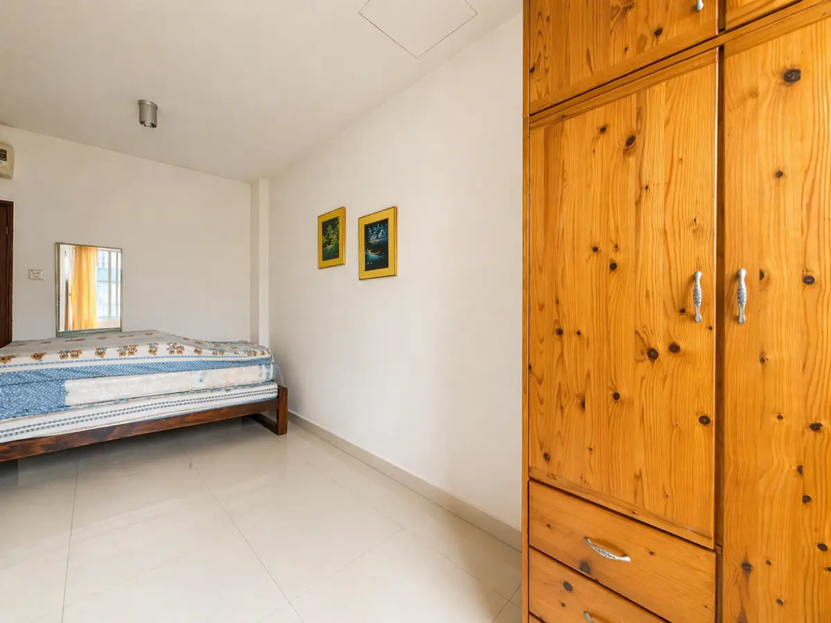 Bedroom with a wooden bed on the left and a tall wooden wardrobe on the right, blue-patterned bedding visible.