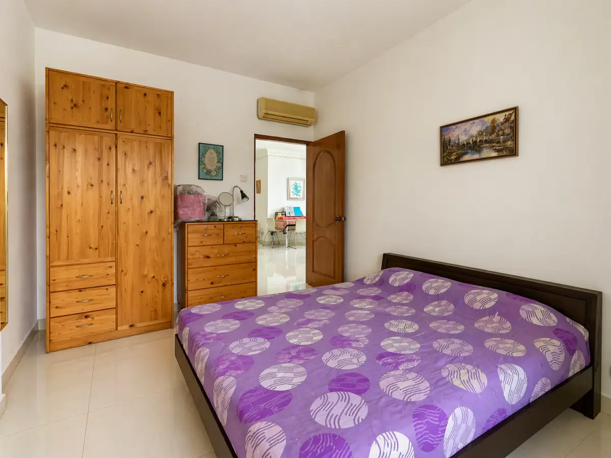 Bedroom with a dark wood bed, purple patterned duvet, and light wood wardrobe and dresser; door open to another room.