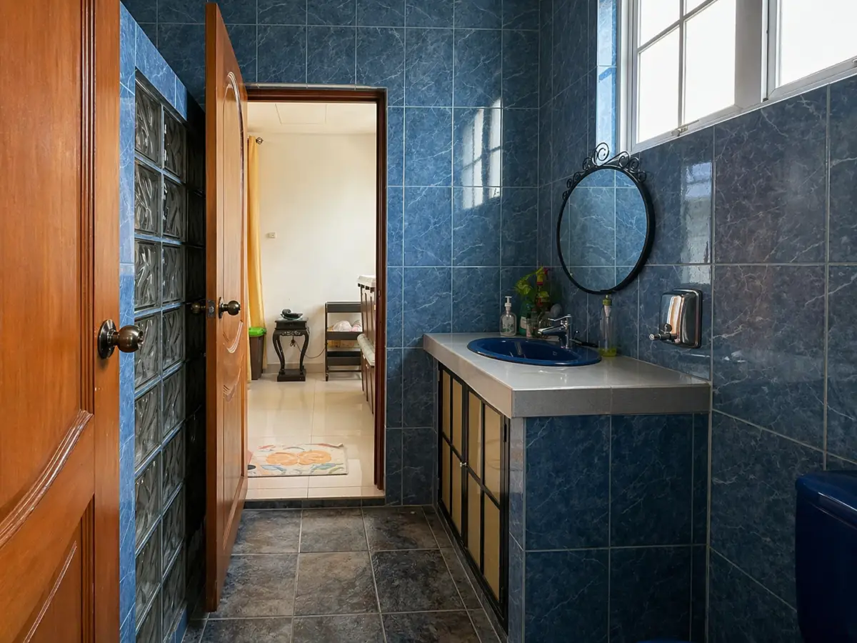 Blue tiled bathroom with a gray countertop sink and a round decorative mirror, open door revealing a bedroom beyond.