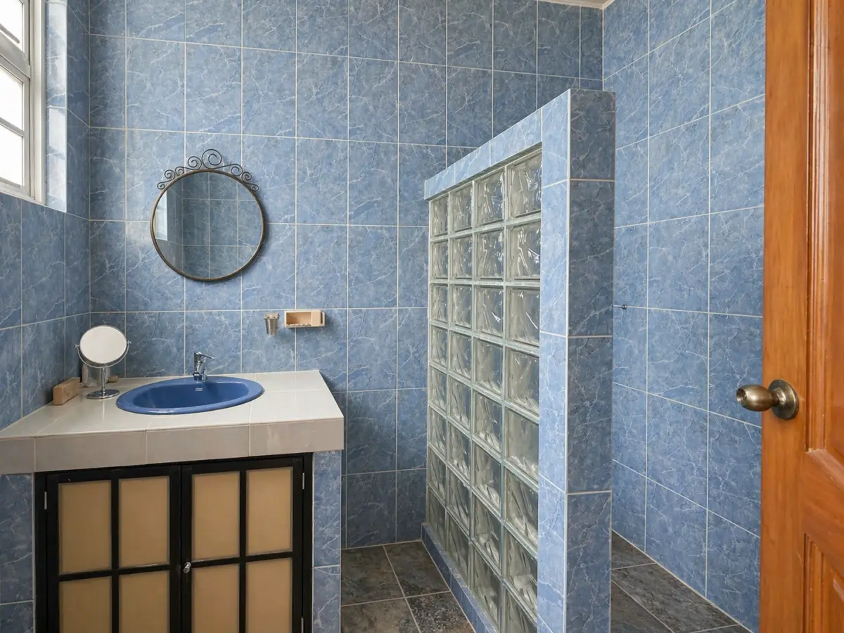 Blue-tiled bathroom with a blue sink, round mirror, and glass-block shower wall.