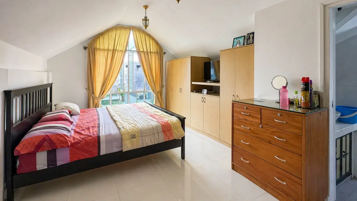 Bright bedroom with a dark wooden bed, colorful quilt, and a large window with yellow curtains.