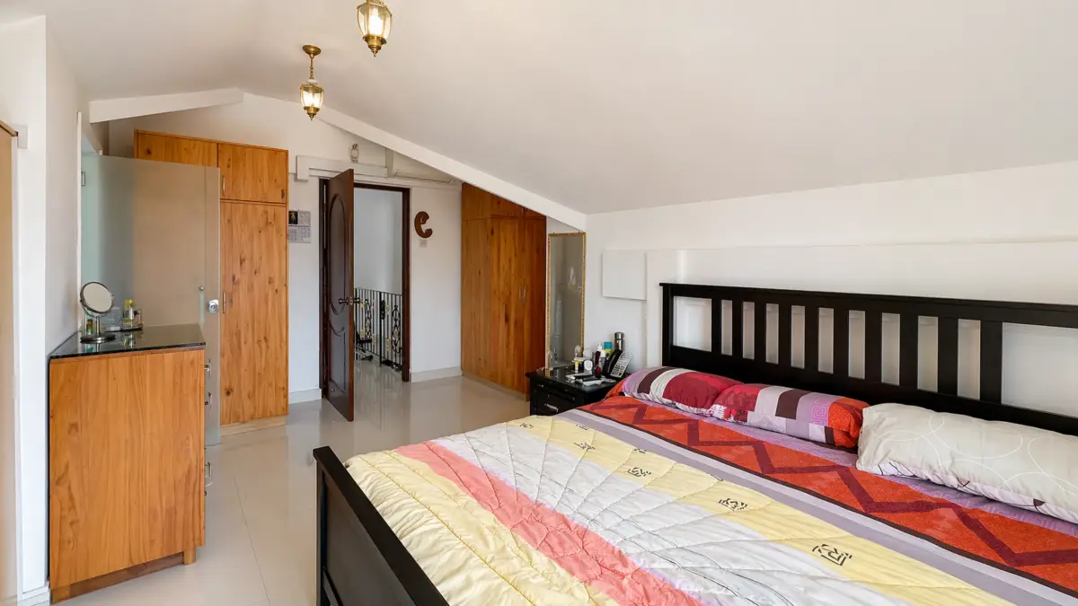 A large bedroom with a dark wooden bed, colorful quilt, and matching wooden wardrobes along the wall under a sloped ceiling