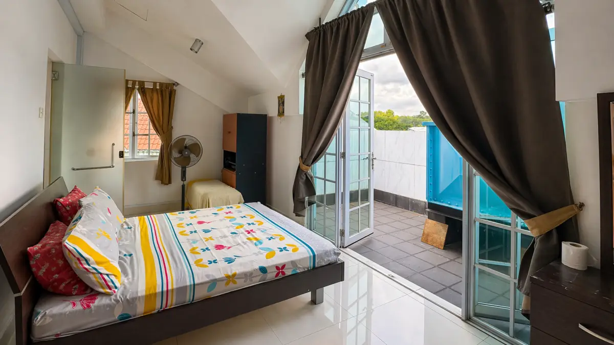 Bedroom with a colorful floral bedspread, a fan, and a balcony door opening to an outdoor terrace on a sunny day
