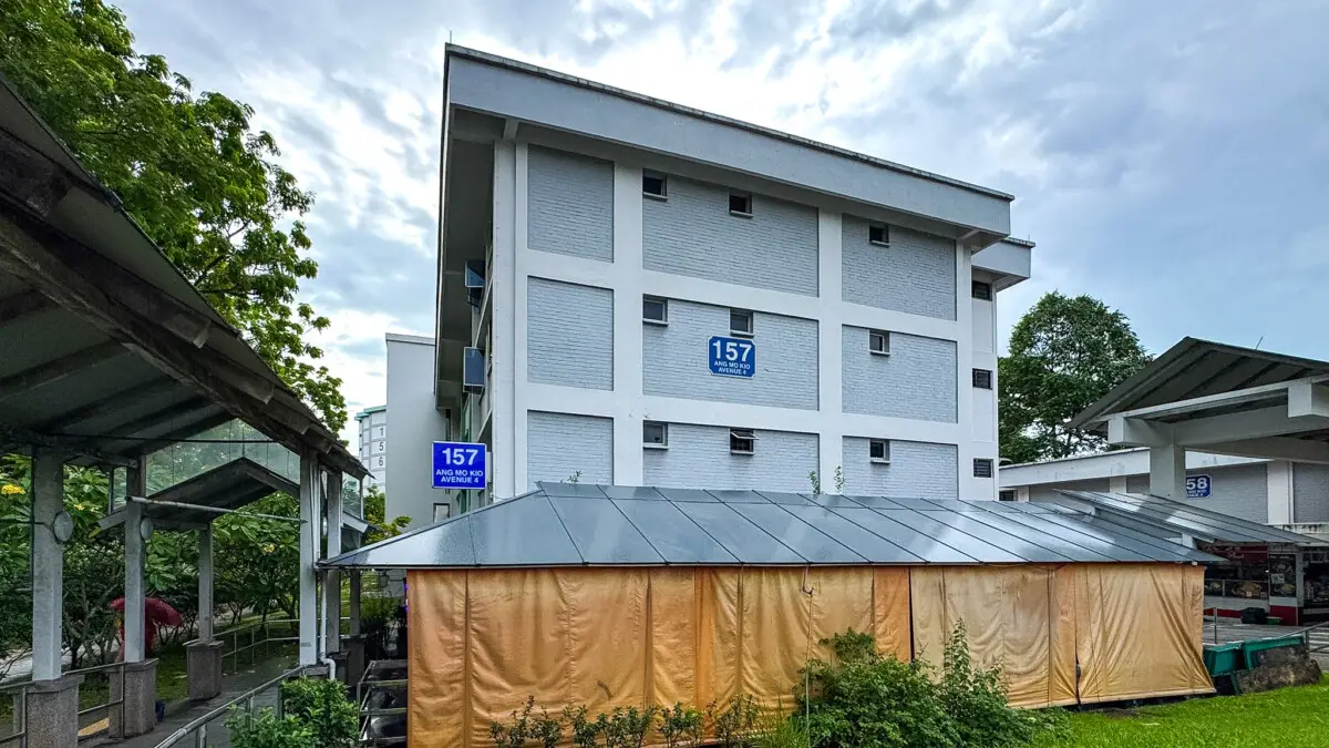 White multi-story building with blue address signs reading 157, and a tan canopy tent in the foreground.